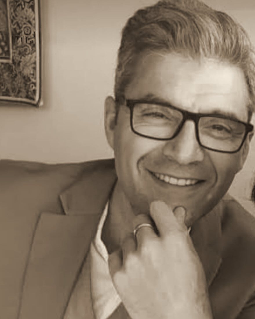 Retrato de Cristóbal Cordero, sonriendo, con gafas y la mano en la barbilla
